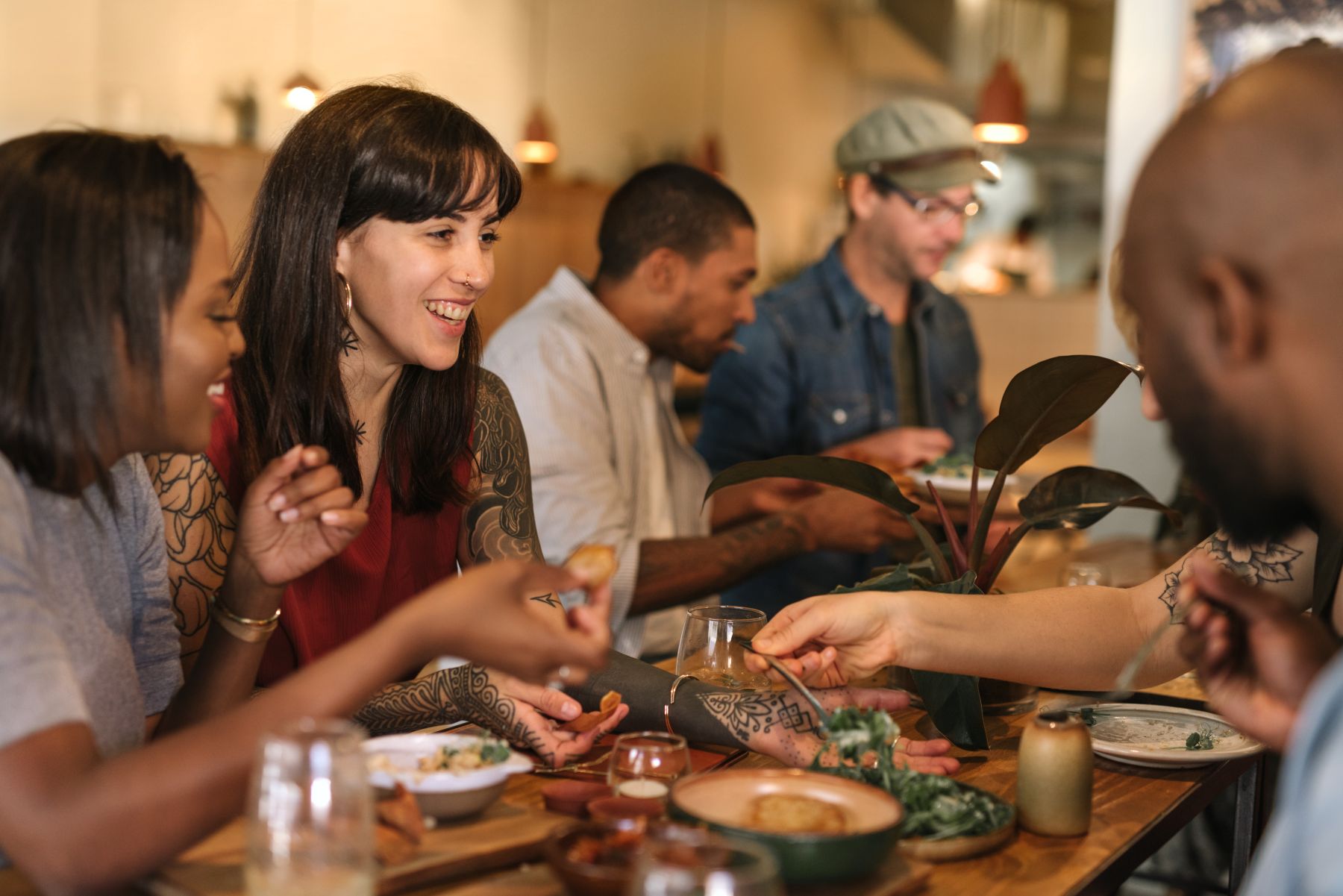 Smiling group of diverse young friends sitting at a table in a trendy bistro enjoying a meal together