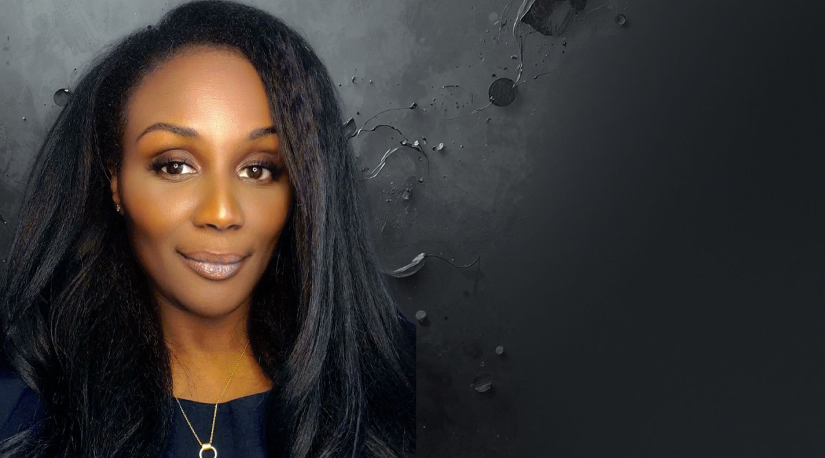 A close-up portrait of a woman positioned on the left side of the image, with a large dark, textured area extending across the right side. She has long, straight black hair, warm brown skin, dark eyes with makeup, and a slight smile. She wears a dark top and a thin gold necklace with a circular pendant. The background is charcoal gray with irregular glossy streaks, droplets, and faint abstract textures.